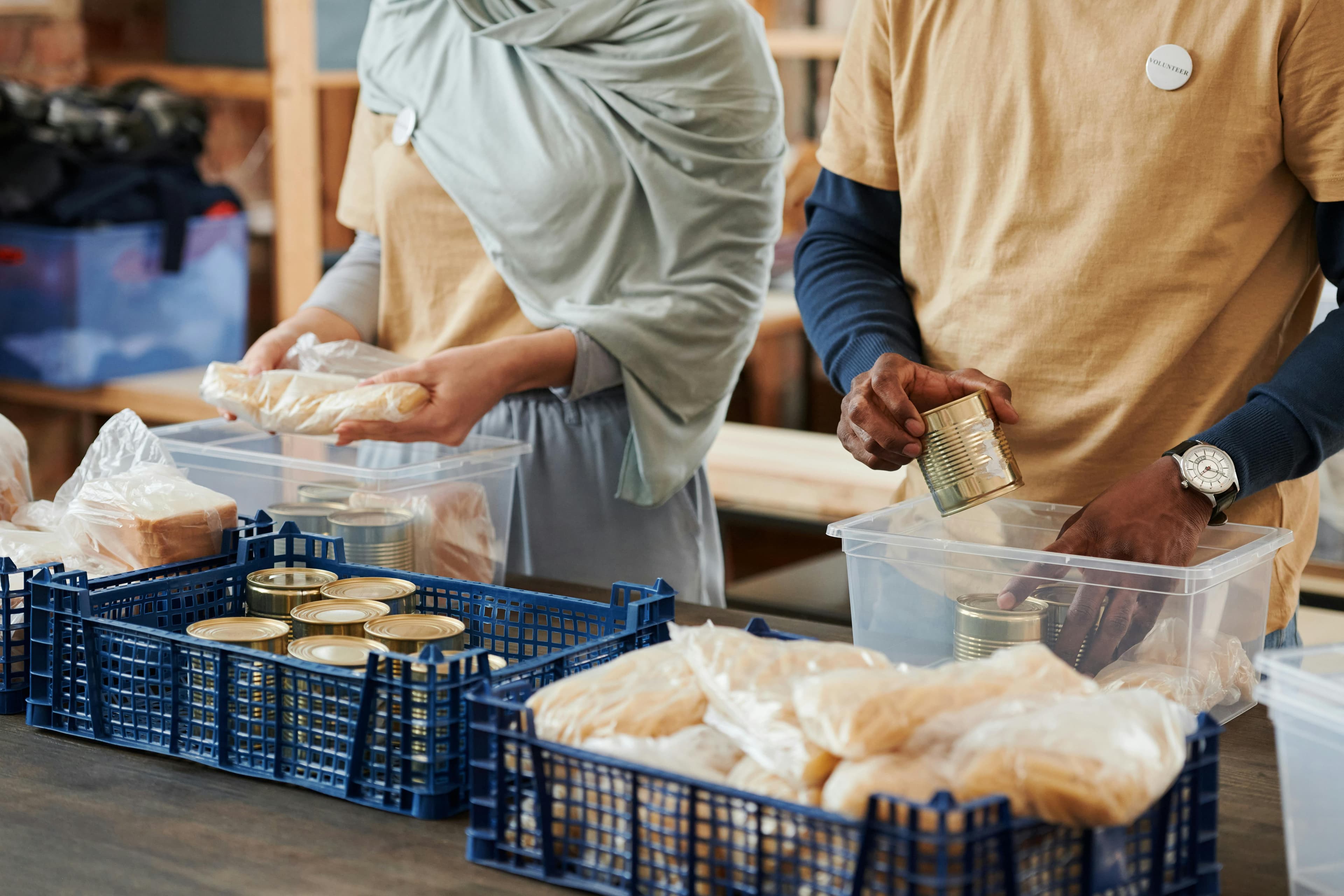 Two volunteers organize food items, including canned goods and bread, in a community service setting.