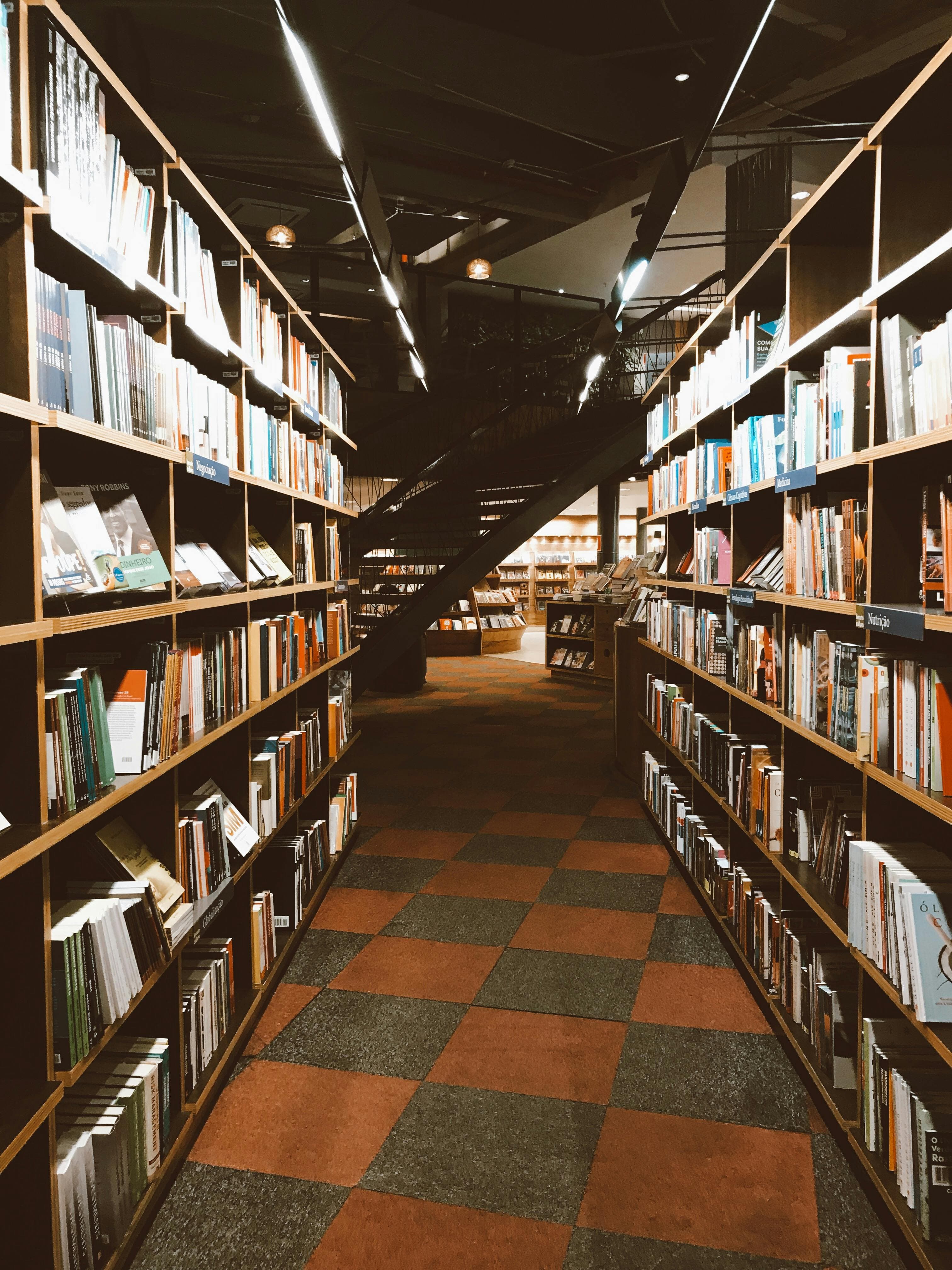 A cozy library corridor lined with bookshelves, leading to a spiral staircase, illuminated by pendant lights.